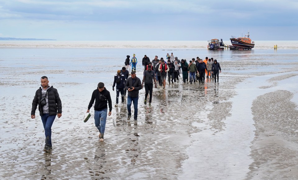 A group of migrants walk ashore in Dungeness, Kent, after being intercepted by a lifeboat on August 25, 2022