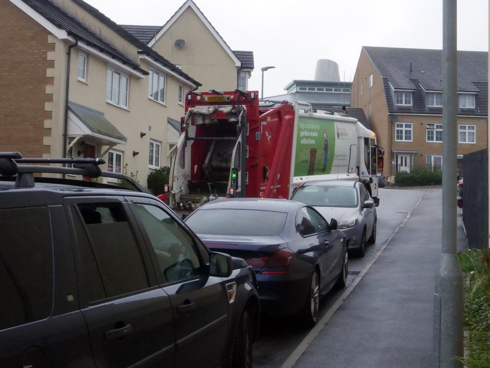 A refuge lorry has trouble swerving between all the parked vehicles on the road