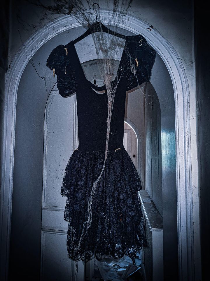 A black cocktail dress hangs creepily in a door frame