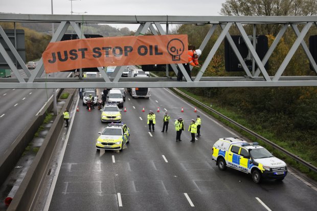 Police watch as traffic is held back as an activist from Just Stop Oil occupies a gantry over the M25 near Godstone in Surrey this morning