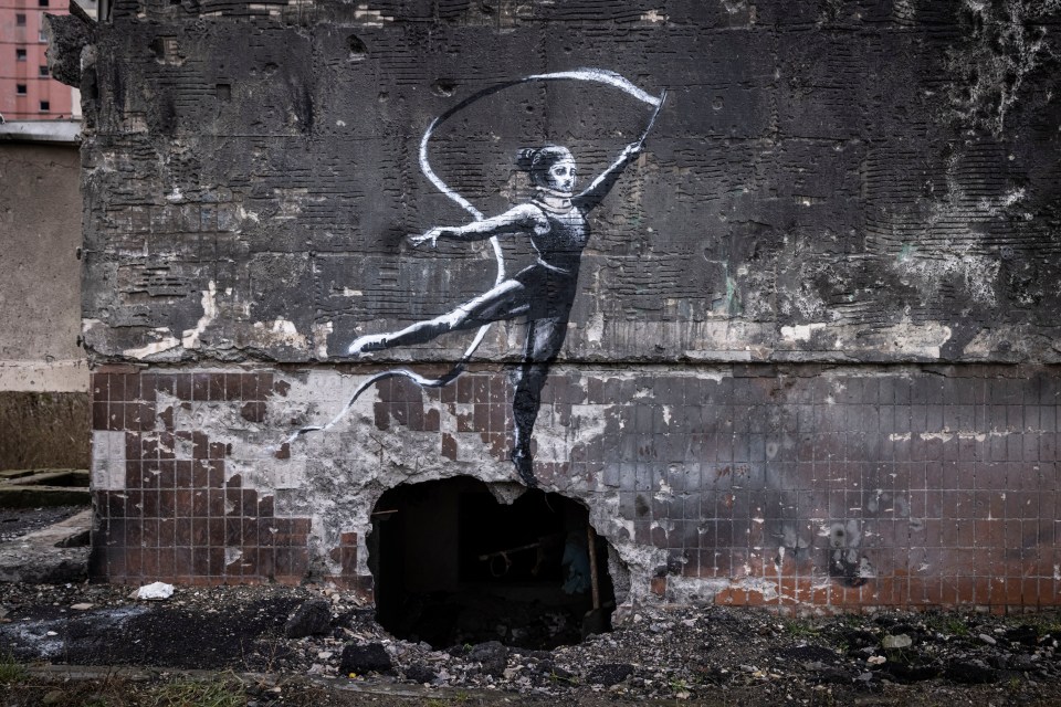 Graffiti of a woman waving a ribbon seen on the wall of a destroyed building in Irpin