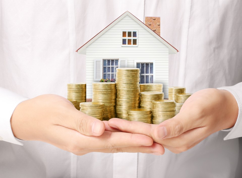 Hands holding stacks of coins in front of a small house model.