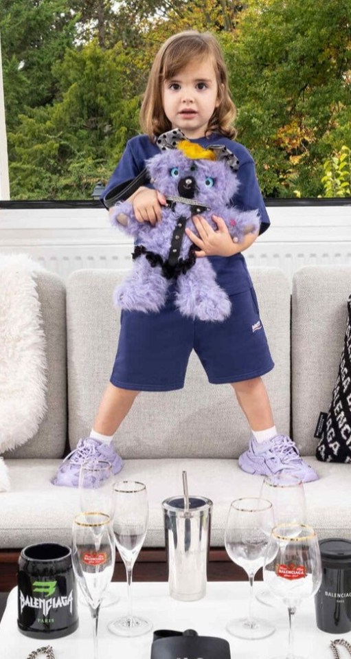 A young girl is pictured holding a teddy bear in bondage-style gear on the gift shop section of the Balenciaga website