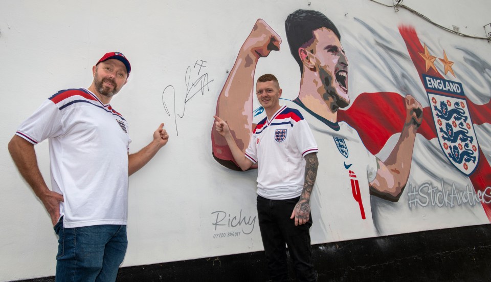 Daniel and mural artist Richy Hughes point to Declan Rice's signature after the West Ham star visited