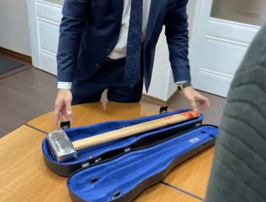 a man in a suit holds a hammer in a violin case