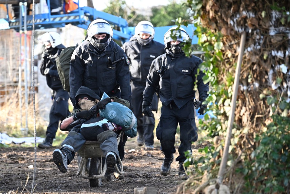 Police officers push a climate activist with a wheelbarrow off the site