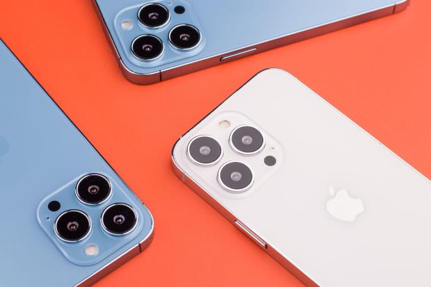 three apple iphones are laying on an orange surface