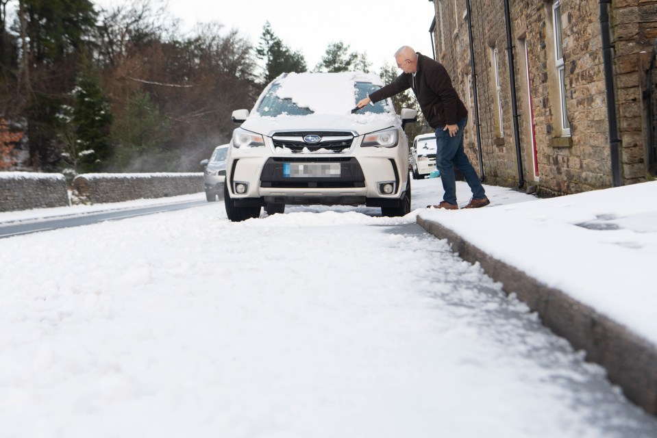 A man wipes snow off his car's windscreen in Nenthead