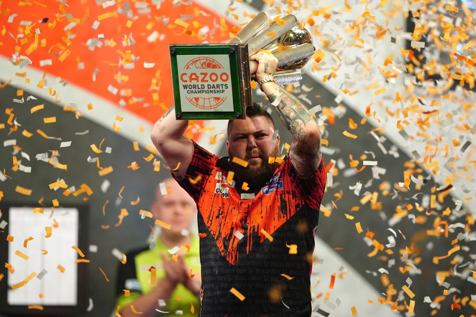 Michael Smith lifts the Sid Waddell trophy for the first time, as Michael Van Gerwen watches on.