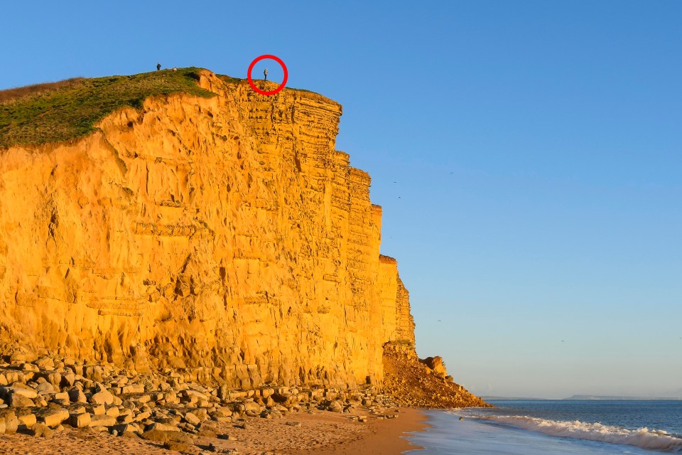 This is the moment a foolhardy tourist risks his life to peer over the edge of a crumbling cliff