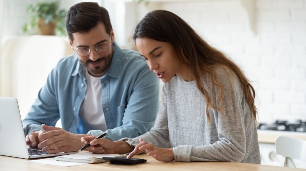 a man and a woman sit at a table looking at a laptop