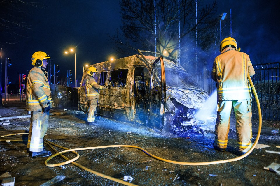 Firefighters douse a burned out police riot van