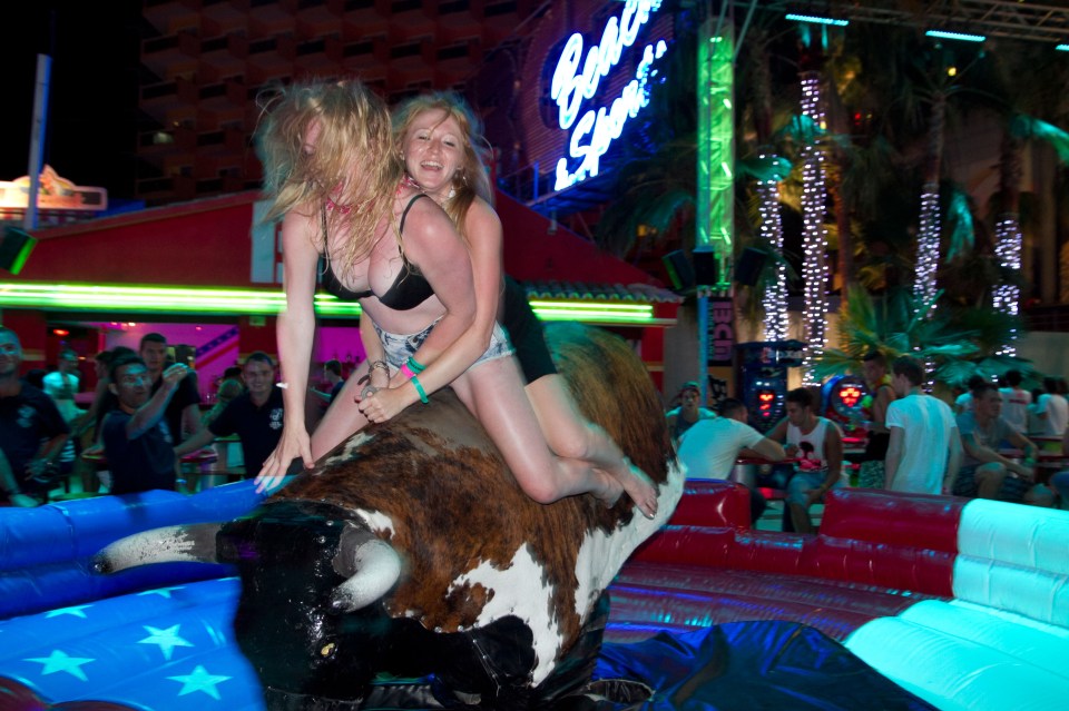 Two pals ride a mechanical bull on the strip