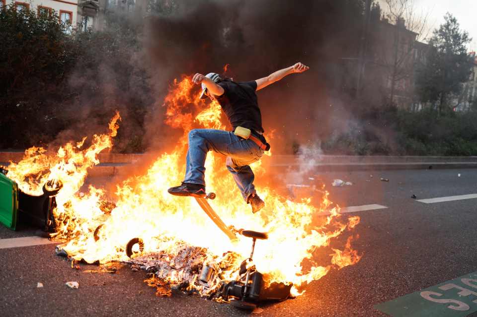 A protestor rides with a skateboard over burning bins in Toulouse, southern France