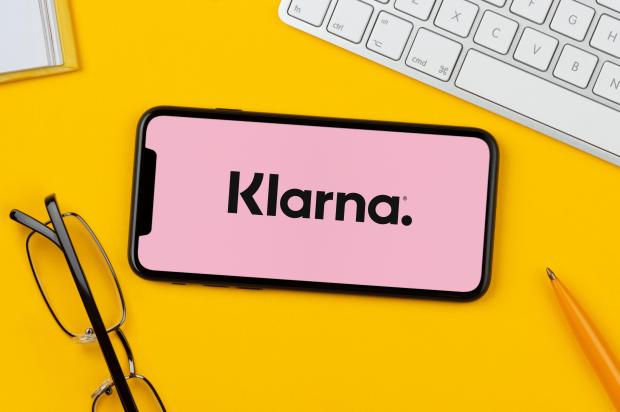 2BH4J54 A smartphone showing the Klarna logo rests on a yellow background along with a keyboard, glasses, pen and book (Editorial use only).