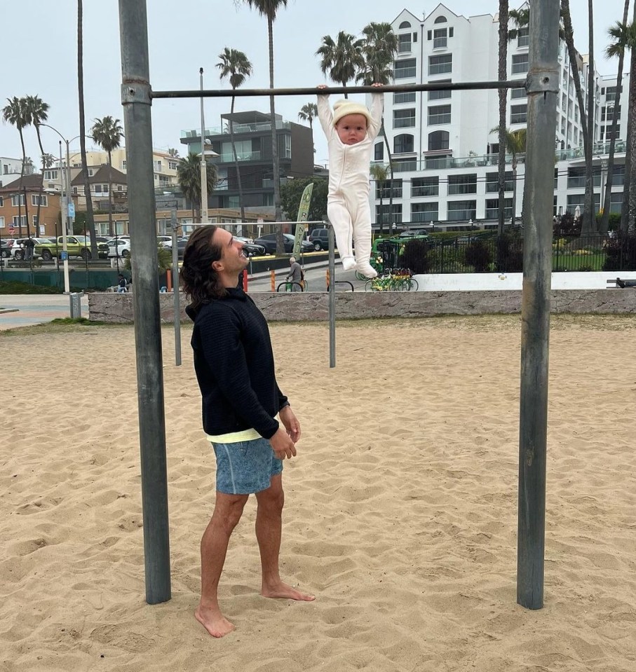 Baby Leni can be seen dangling from a metal bar all on her own, while the fitness guru, 37, proudly observes