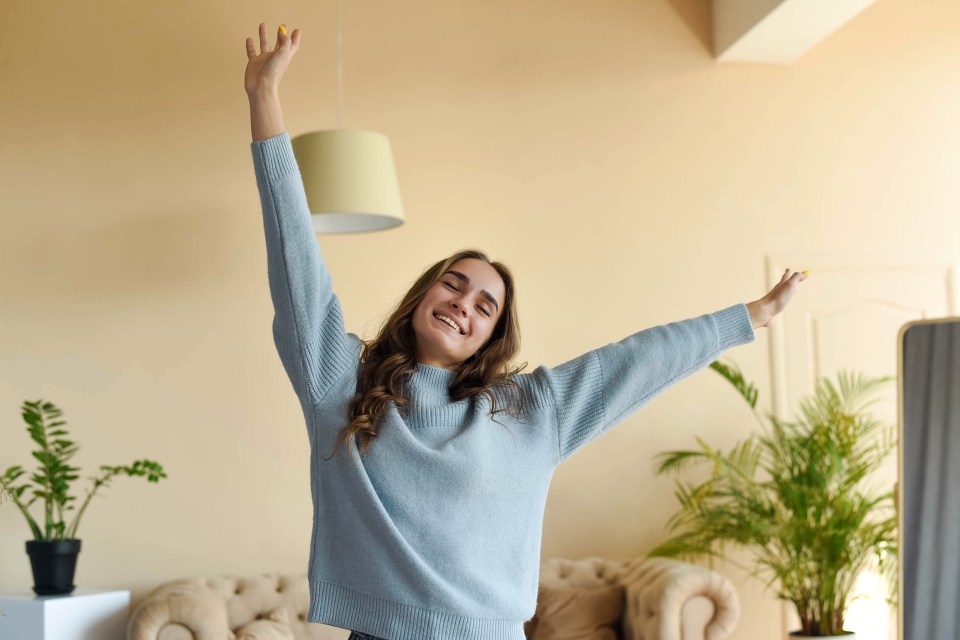 A beautiful girl in a blue sweater is stretching in the room. Morning rituals.