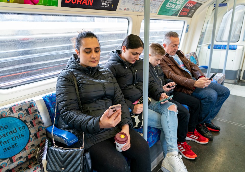 Commuters on the Tube look at their phones as the alarm goes off