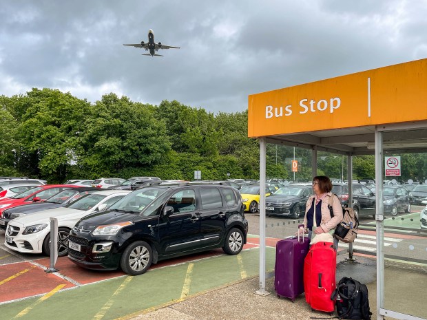 a woman waits at a bus stop while a plane flies overhead