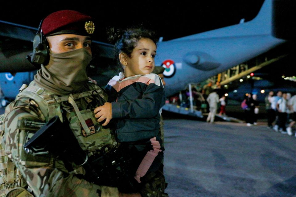 A soldier carries a child as people evacuated from Sudan disembark from an aircraft at a military airport in Amman today