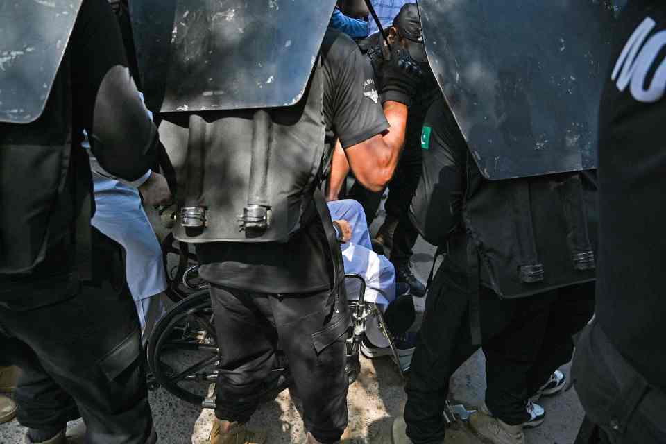 Khan, who is in a wheelchair after fracturing his leg, was escorted to a waiting truck