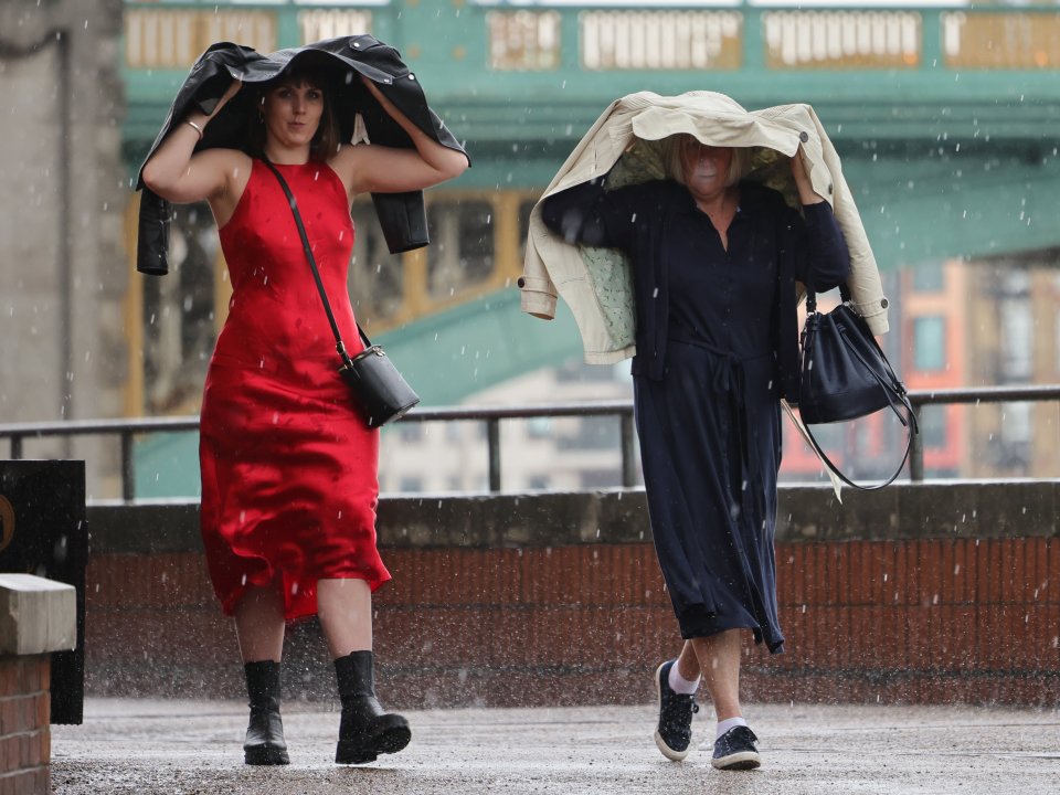 Two women scarper along the banks of the Thames as torrential rainfall batters the capital