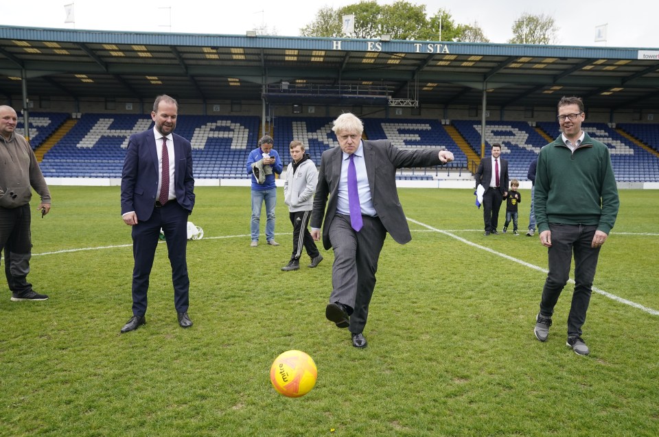 BURY, ENGLAND - APRIL 25: UK Prime Minister Boris Johnson (centre) kicks a football during a visit to Bury FC at their Gigg Lane ground, Bury, Greater Manchester, England. (Photo Danny Lawson - WPA Pool/Getty Images)