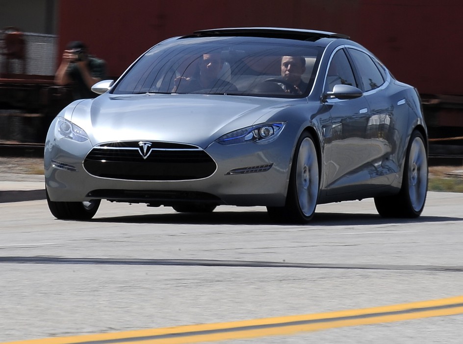 Tesla Motors Chairman and CEO Elon Musk (in driver's seat) and chief designer Franz von Holzhausen (in passenger seat) drive the new Tesla Model S all-electric sedan out into the street as members of the media look on, at the car's unveiling in Hawthorne, California on March 26, 2009.  Musk said the state-of-the-art, five-seat sedan will be the world's first mass-produced, highway-capable electric car.  The car has an anticipated base price of 57,400 US dollars but will cost less than 50,000 after a federal tax credit of 7,500 dollars.   AFP PHOTO / Robyn BECK (Photo by Robyn BECK / AFP)        (Photo credit should read ROBYN BECK/AFP via Getty Images)