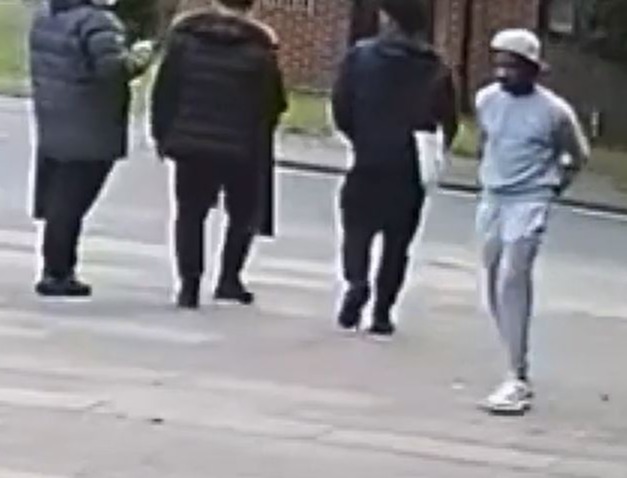 A man - dressed in a light-coloured tracksuit - walks past the group with his hands behind his back