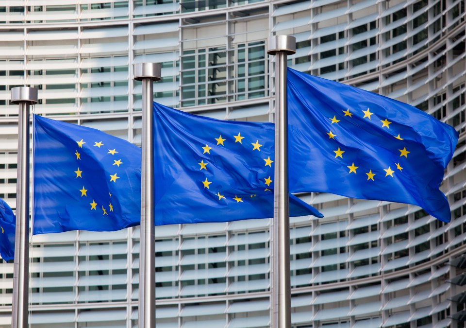 Three European Union flags waving in front of a building.