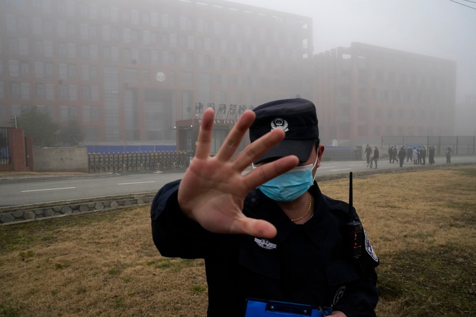 A security guard moves journalists away from the Wuhan lab during a visit from the WHO