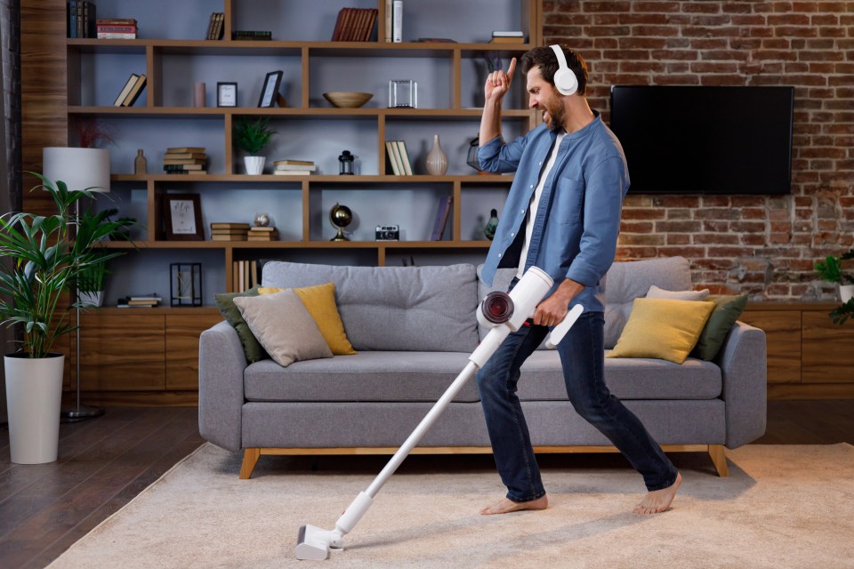 Cheerful guy, the man cleans the apartment. Vacuuming, wearing headphones with dancing and singing into a smartphone instead of a microphone. House cleaning is easy