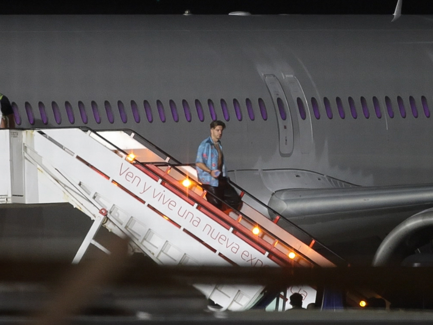 Grealish departs the plane in an open blue shirt and gold chains