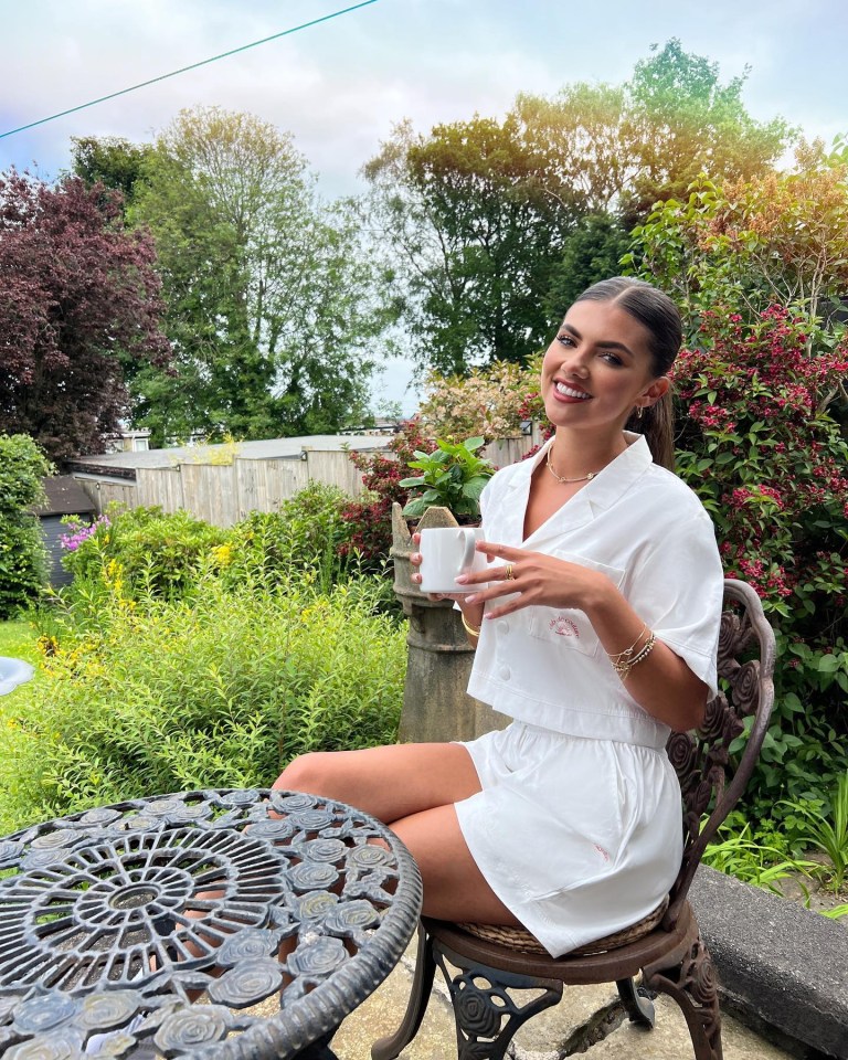 She sat at the garden table dressed in all white as she smiled while holding a cuppa