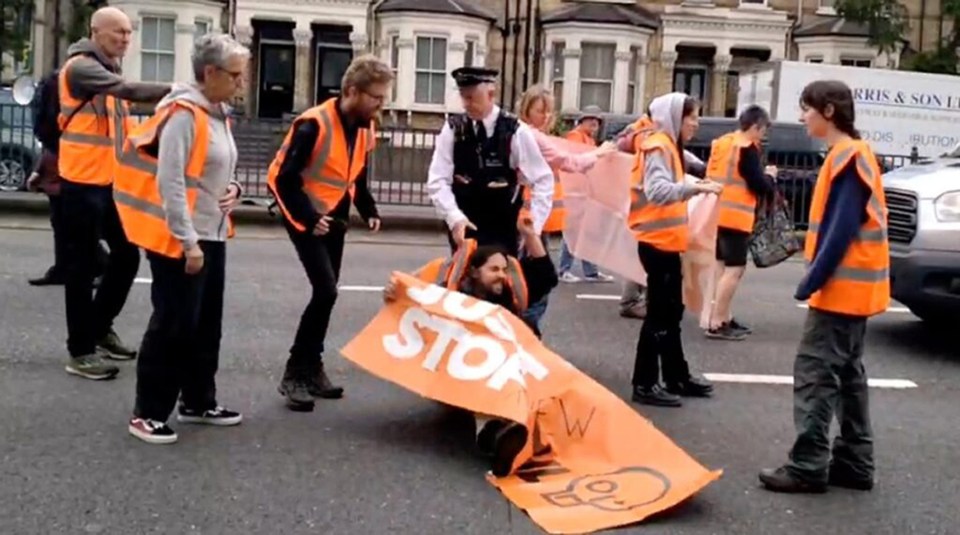 A policeman drags an activist along the ground during their slow walk protest in west London