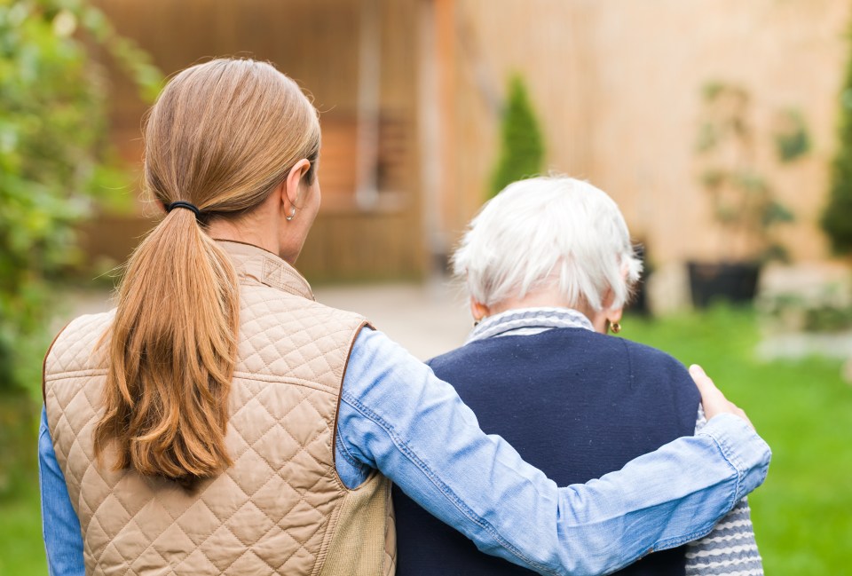 A stock image of a young carer walking with an elderly woman through a park