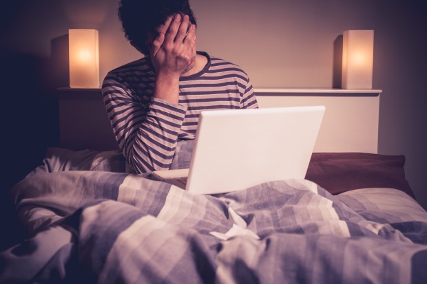 a man covering his face while using a laptop