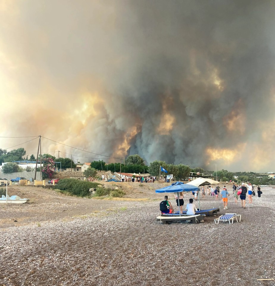 Tourists take shelter on a beach as thick black smoke fills the sky from the wildfires on Rhodes