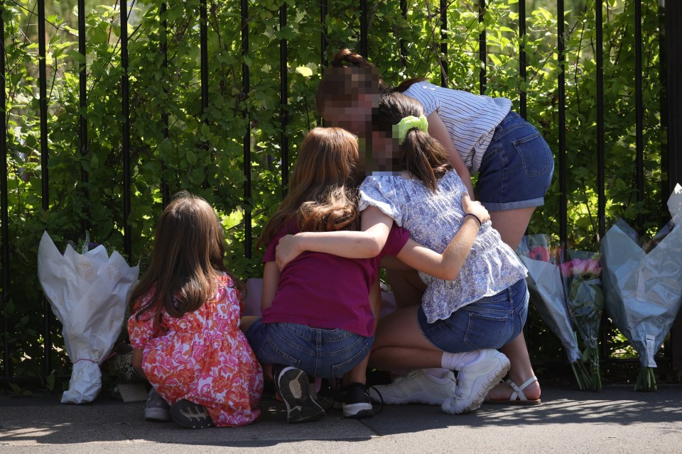 A group of children embrace as they leave flowers and a stuffed animal outside The Study Prep school