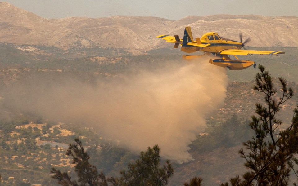 A firefighting plane drops water over a wildfire burning near Asklipio