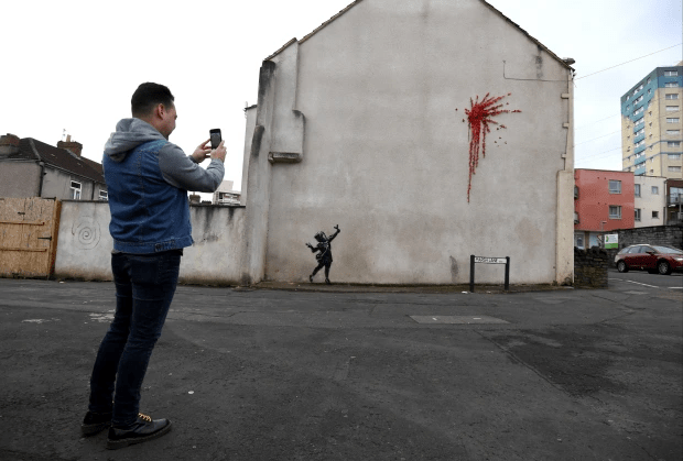 Banksy graffiti shows a girl with a slingshot catapulting flowers in Bristol