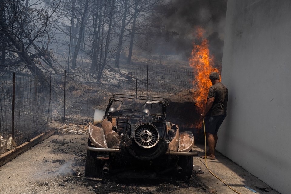 A local desperately tries to extinguish the flames surrounding his home on Rhodes