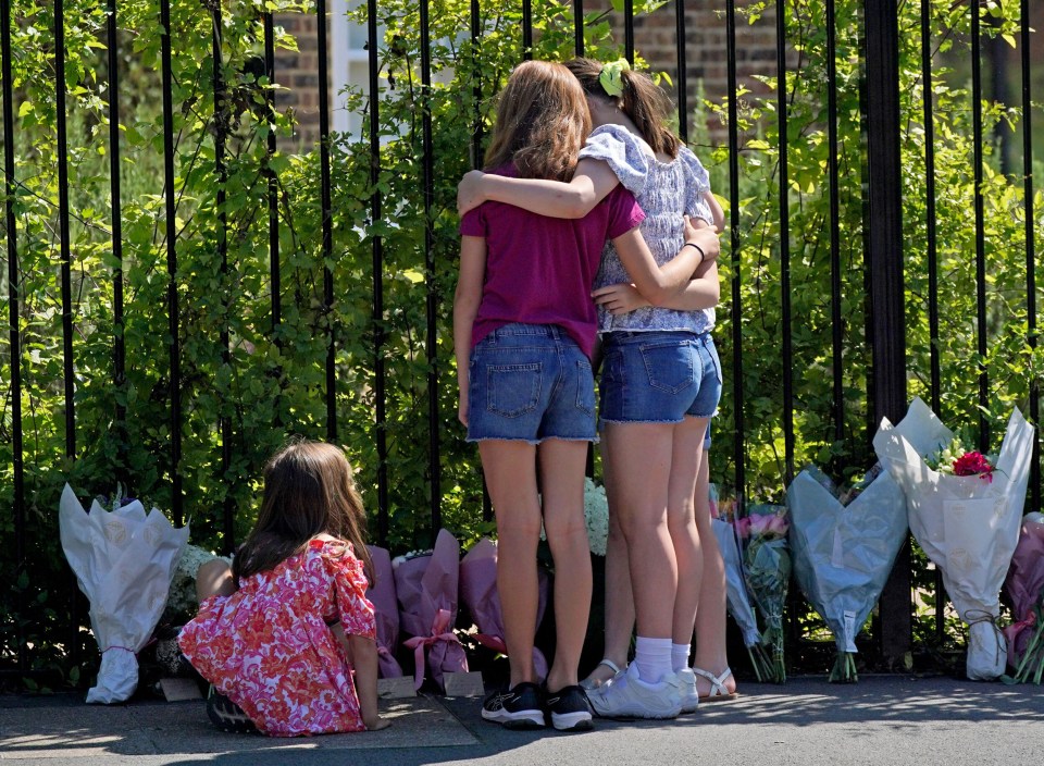 A group of children embrace as they leave flowers and a stuffed animal outside The Study Prep school