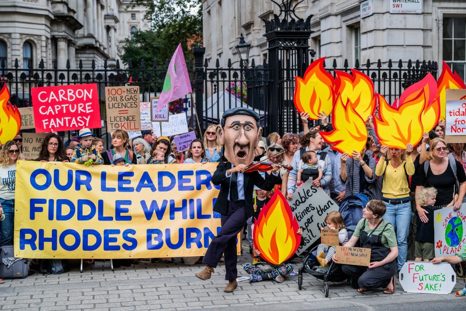 Mandatory Credit: Photo by Guy Bell/Shutterstock (14039527d) A fiddling 'Rishi' dances in front of the protest which is largely made up of mothers worried about the future for their children - Our Leaders Fiddle While Rhodes Burns Action by Mothers and joined by Extinction Rebellion outside Downing Street. It is in protest to Prime Minister Rishi Sunak allowing new North Sea Oil and Gas licences. Mothers protest as Our Leaders Fiddle., Downing Street, London, UK - 03 Aug 2023