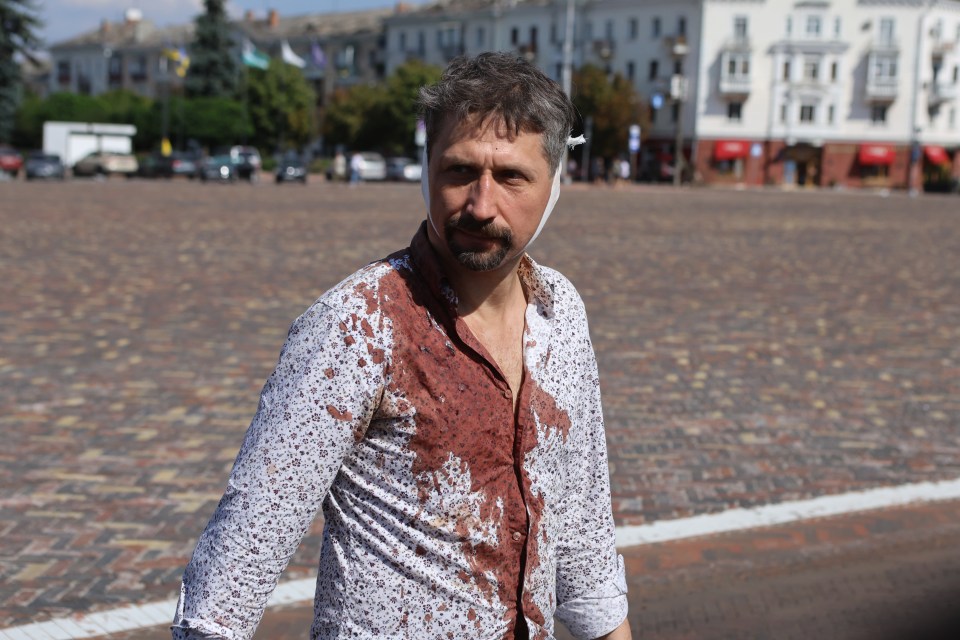 A wounded man in a bloody shirt walks across a square in front of the theatre building damaged by Russian shelling, where people were hiding from bombs