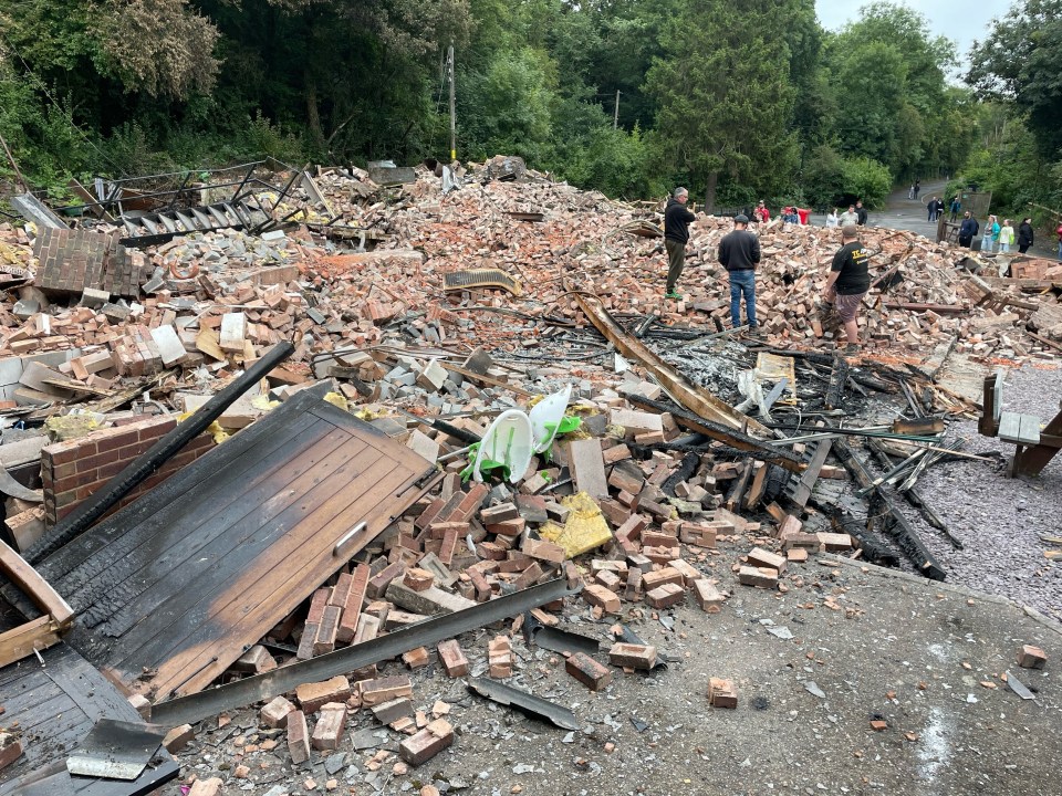 Locals inspect the rubble remains of The Crooked House which has been demolished two days after it was gutted by fire