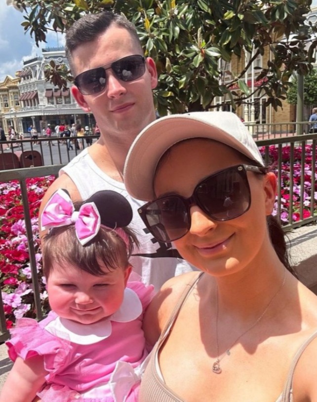 a woman wearing sunglasses holds a baby in a pink dress