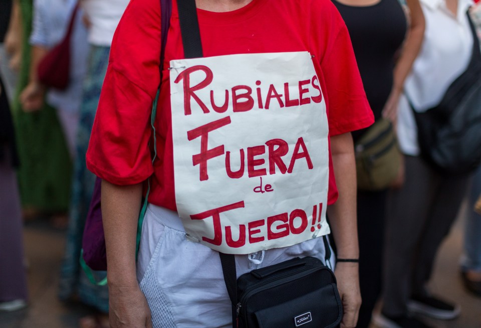 Protestor wearing a red shirt with a sign reading "Rubiales Fuera de Juego!" in Spanish.