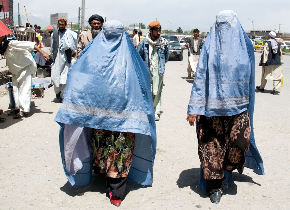 Two burka-clad women cover up in Kabul under the regime's strict public dress code