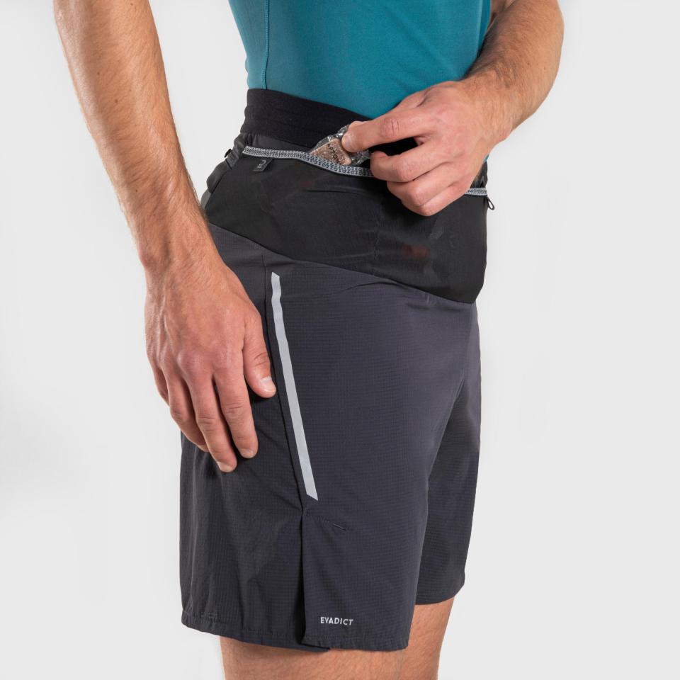 Man placing energy gel in the pocket of dark grey trail running shorts.